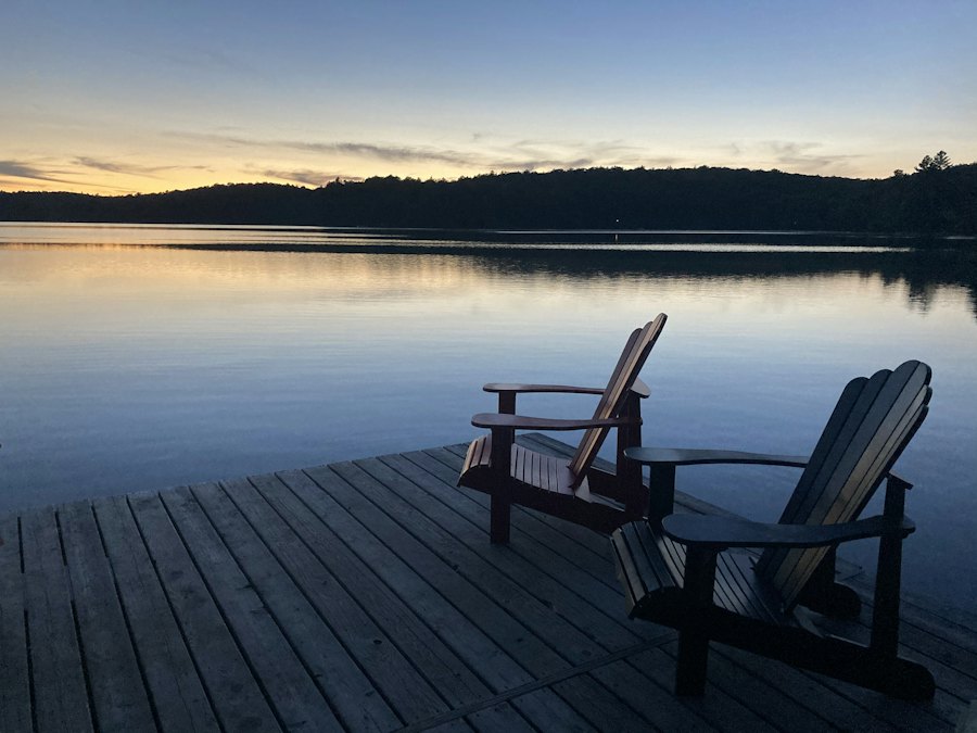 Two empty chairs on a lake dock at dusk